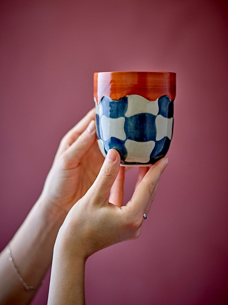 Check cup in blue and cream checkered stoneware with red rim, held in hand
