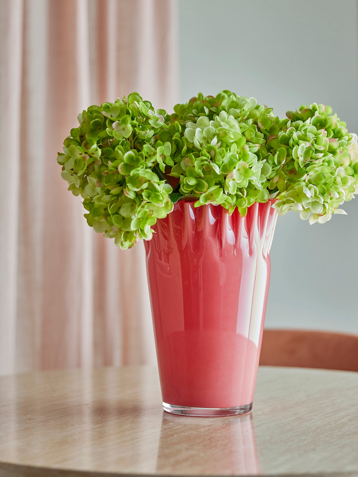 Janine coral red glass vase filled with green hydrangeas on a wooden table