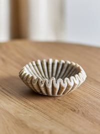 Harmonia beige marble bowl on a light oak table with a soft blurred window behind