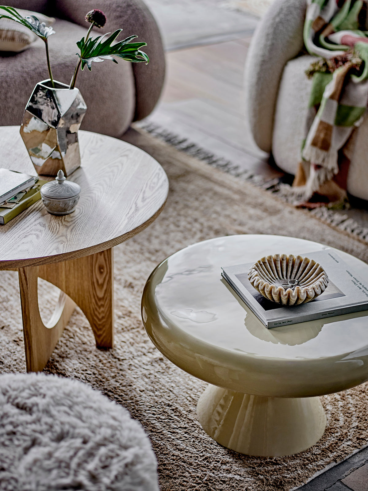 Small Harmonia marble bowl on a stack of books on a glossy cream side table, beside a round oak table and a silver vase of stems