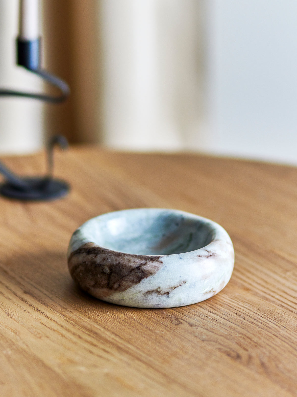 Indah grey marble bowl on a light oak table beside a black candle holder and blurred cream curtain