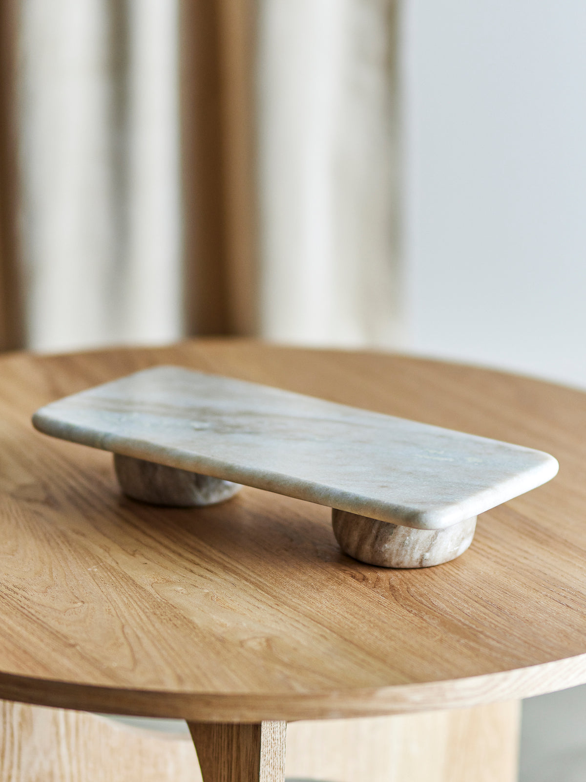 Fatin marble pedestal on a round oak table in front of a soft neutral curtain