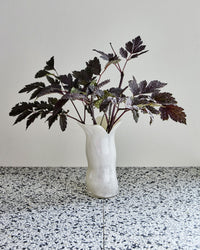 House Doctor Cuff off-white glass vase with dark foliage on a terrazzo surface