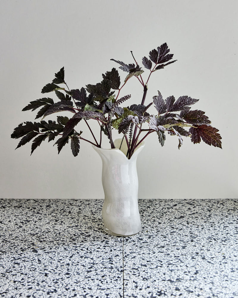 House Doctor Cuff off-white glass vase with dark foliage on a terrazzo surface