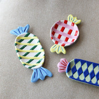 small round candy-shaped ceramic plate in pink and red check with yellow ends
