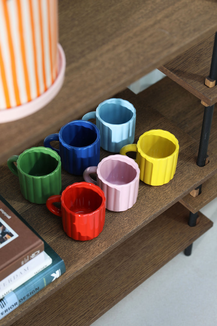 set of colourful tube espresso mugs styled on shelving unit
