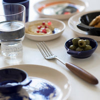 a table set-up of ottolenghi crockery and glassware showing what can be achieved when putting different colours of tableware together with blues, whitesk, and the multi-colour joy of the hand painted face print