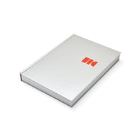 HKLIVING Limited Edition Lookbook 2026-2027, closed hardback book with mirrored silver foil cover, top corner angle showing the red logo mark
