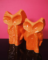 Two orange owl vases against a pink background