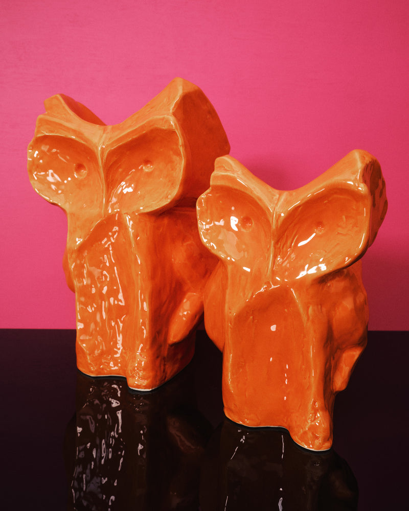 Two orange owl vases against a pink background