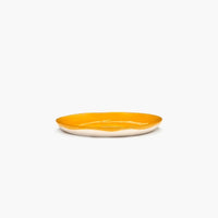 side of the yellow and white side plate from ottolenghi and serax showing the bright yellow pouring over half way down the lip bringing fun and joy to any dinnertable or party with friends