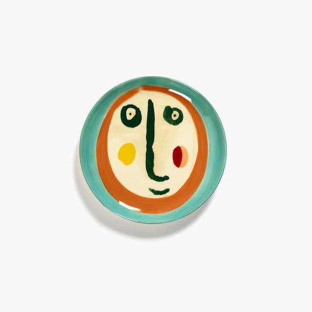 small plate with the ottolenghi face handpainted in azure, yellow, orange, green and black on an off white background