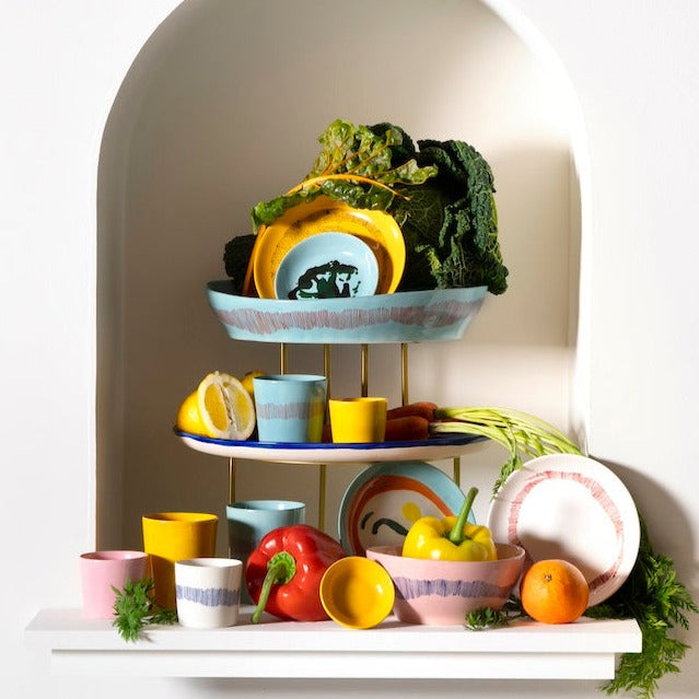 a mixture of colours of dinner ware plates, bowls, and cups from the ottolenghi range including delicious pinks, azure and deep blue, and yellow along with vegetables you'd find in ottolenghi's recipes