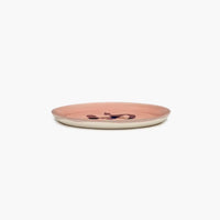 side view of the ottolenghi delicious pink lunch plate revealing the white ceramic and barely revealing the bell pepper design on the top of the plate over the shallow lip of this searx produced dinnerware