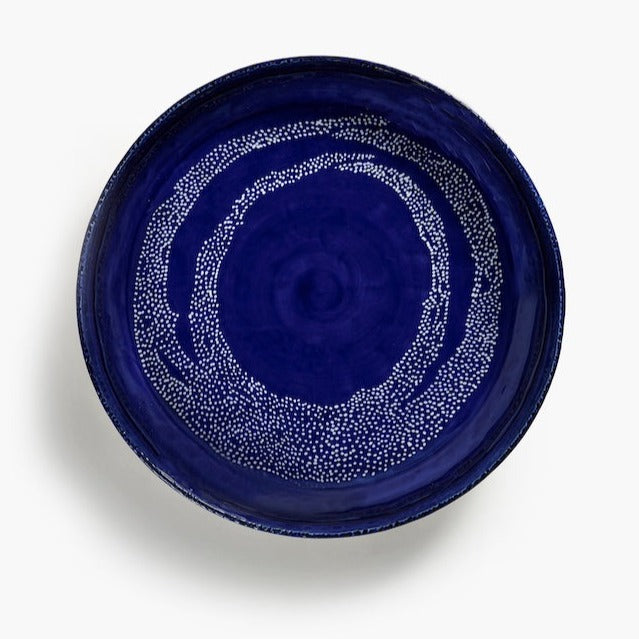 a deep blue bowl with white dots showing clearing the hanpainted nature of the large serving dish and gleaming with a generous aount of glaze making it hard wearing and perfect for dinner parties and feasts with the family: a piece of tableware you'd pass. down the generations