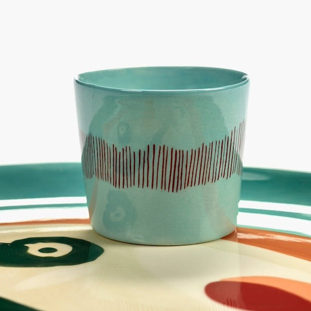 azure blue with red striped espresso cup on a plate with handpainted face in ottolenghi's indomnitable style