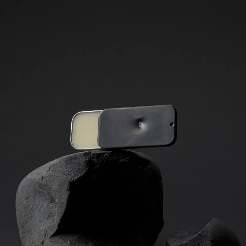 a block of solid fischersund no.8 fragrance in its hand finished tin balanced precariously on a black rock