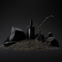 a black bottle of flotholt perfume stood on a sandy hill with black rocks around it