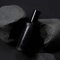 a black spray bottle of the handmade flotholt fragrance creaking out of a blakc rock