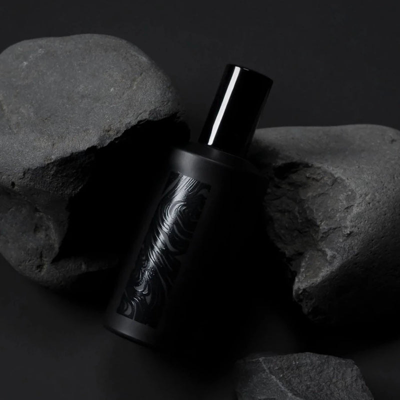 a black spray bottle of the handmade flotholt fragrance creaking out of a blakc rock