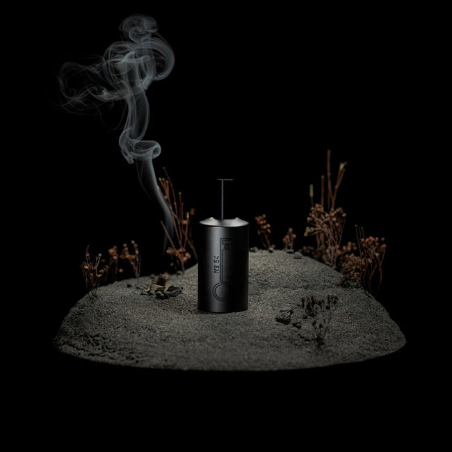 bottle of fischersund number 54 eau de parfum stood on a model of an island with woody plants and an incense stick burning looking like a camp fire