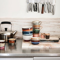 a kitchen set-up with a range of items form hklivings 70s collection including bowls and mugs with a ready brewed kettle, dish of sugar and kitchen kives hanging on the wall behind