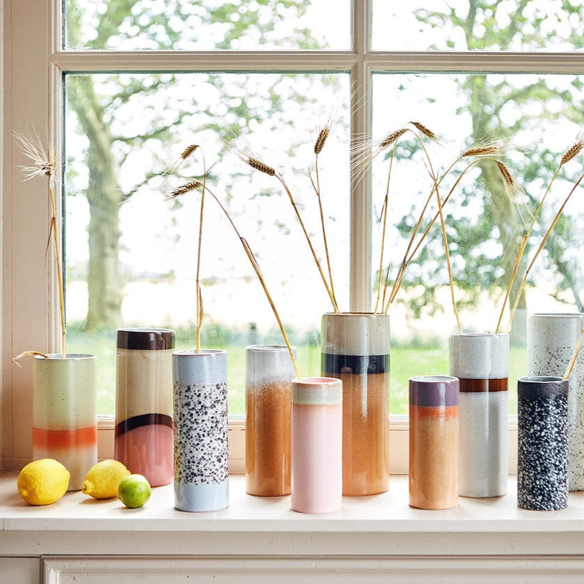 windowsill with a number of different coloured hklinving vases with dried grasses and wheat decorting them