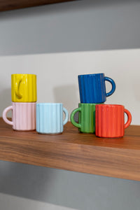 stacked tube espresso mugs in bright colours on wooden shelf
