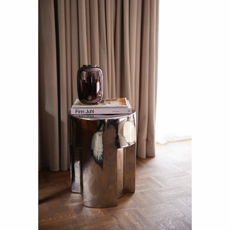 shiny brown metalic vase stood on a couple of books, all atop a shiney metalic silver stool or side table