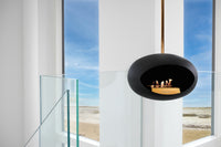 Modern black fireplace pendant in a room with large windows overlooking a beach.