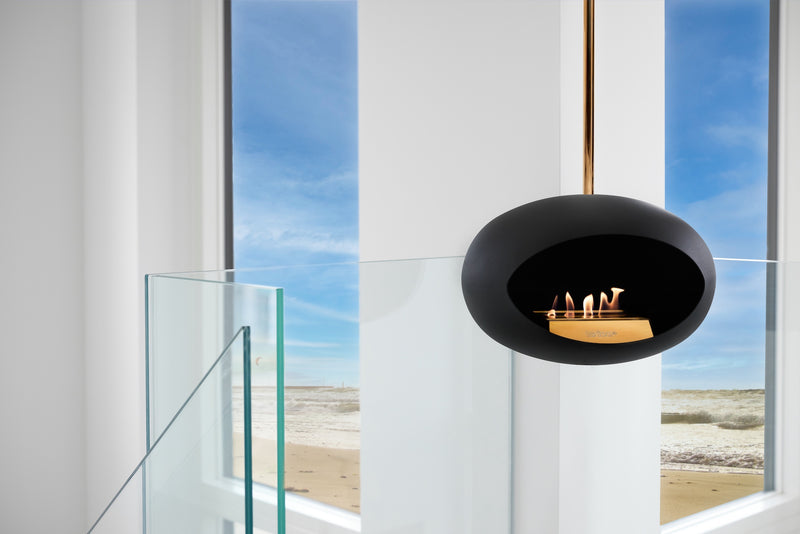 Modern black fireplace pendant in a room with large windows overlooking a beach.