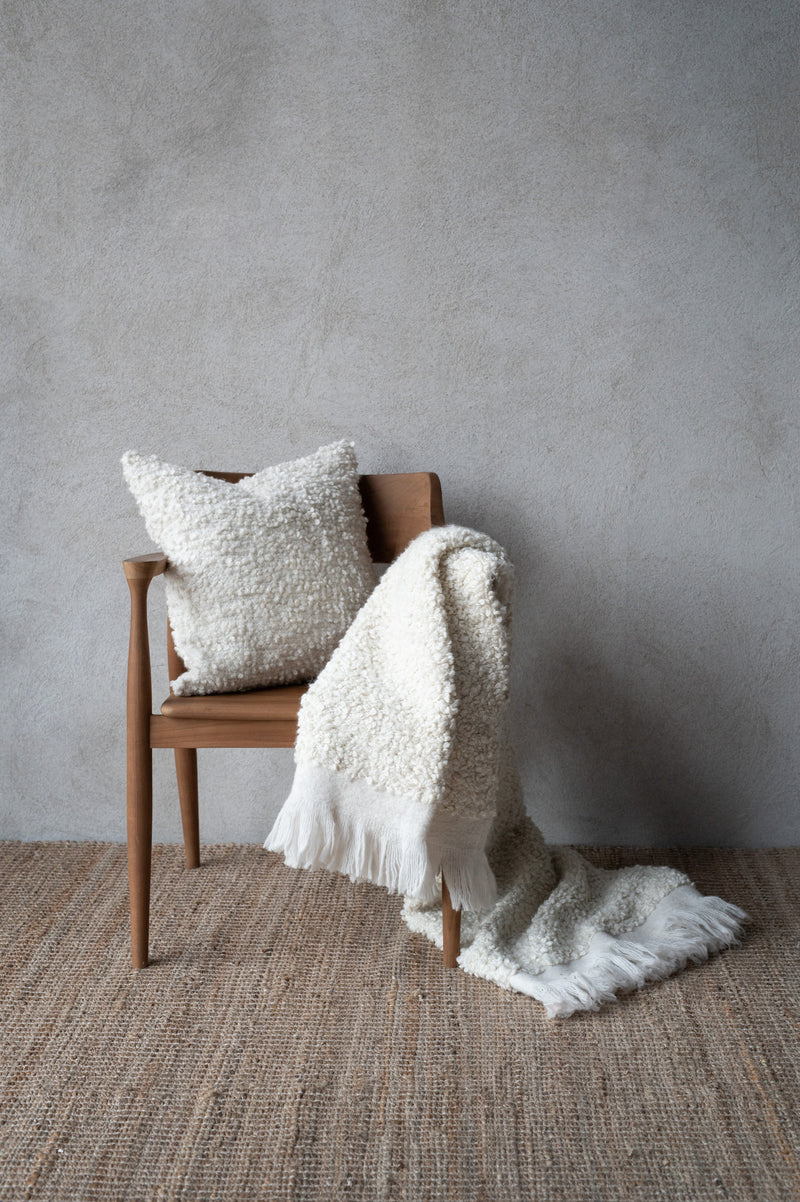 Cosy throw layered with matching cushion in Nordic setting