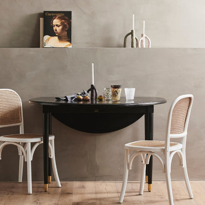 black table with golden feet set up for an afternoon snack against a wall with 3 different colours of the mangrove style trees with candles in them