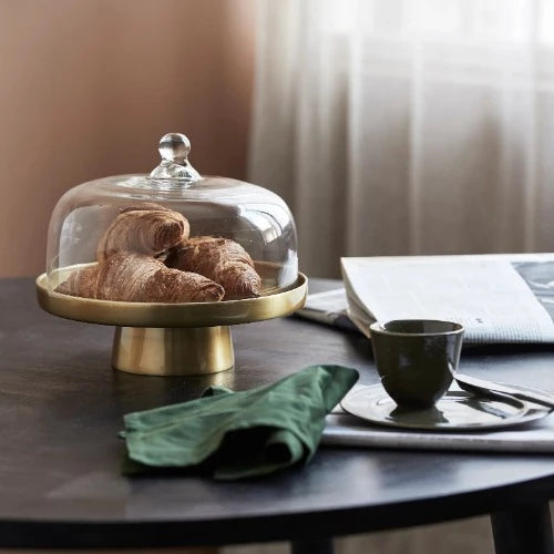 the glass domed, golden, brass cake stand with croisasnts sitting happily under the cloche. All on a table where someone has just finished their breakfast and reading a newspaper