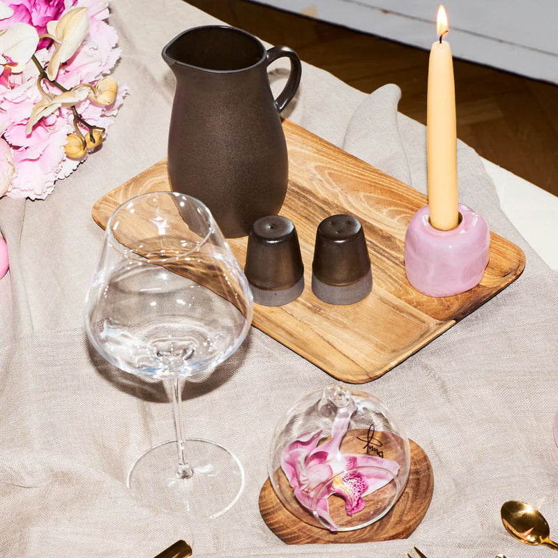 Table setting with wine glass, pitcher, and decorative items on a wooden board.