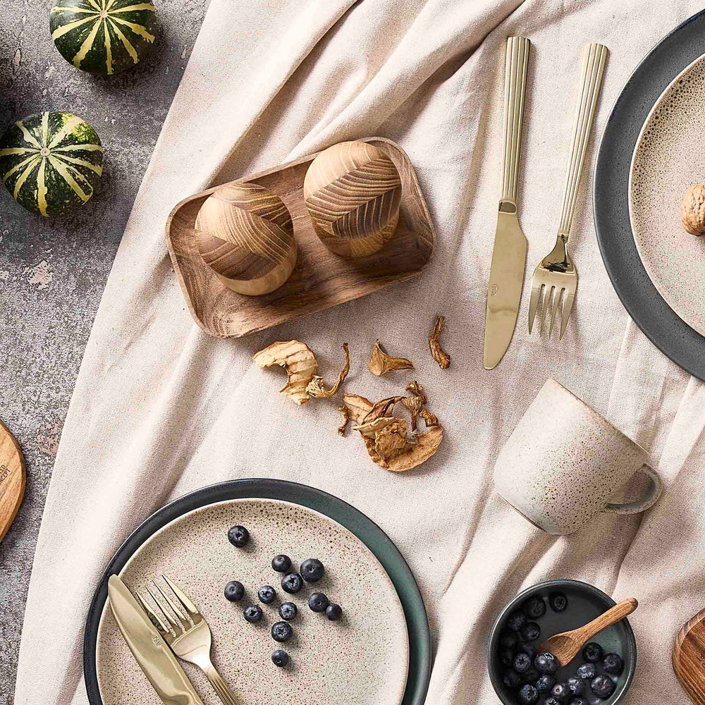 Table setting with ceramic plates, wooden bowls, and cutlery on a textured surface.
