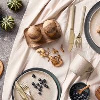Table setting with ceramic plates, wooden bowls, and cutlery on a textured surface.