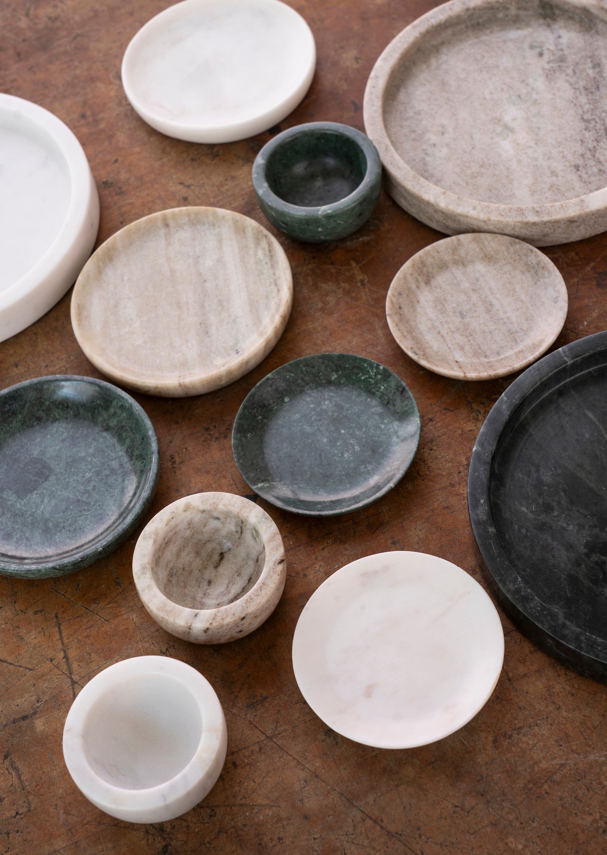 assorted marble trays and small bowls in beige white and green tones on a wooden surface
