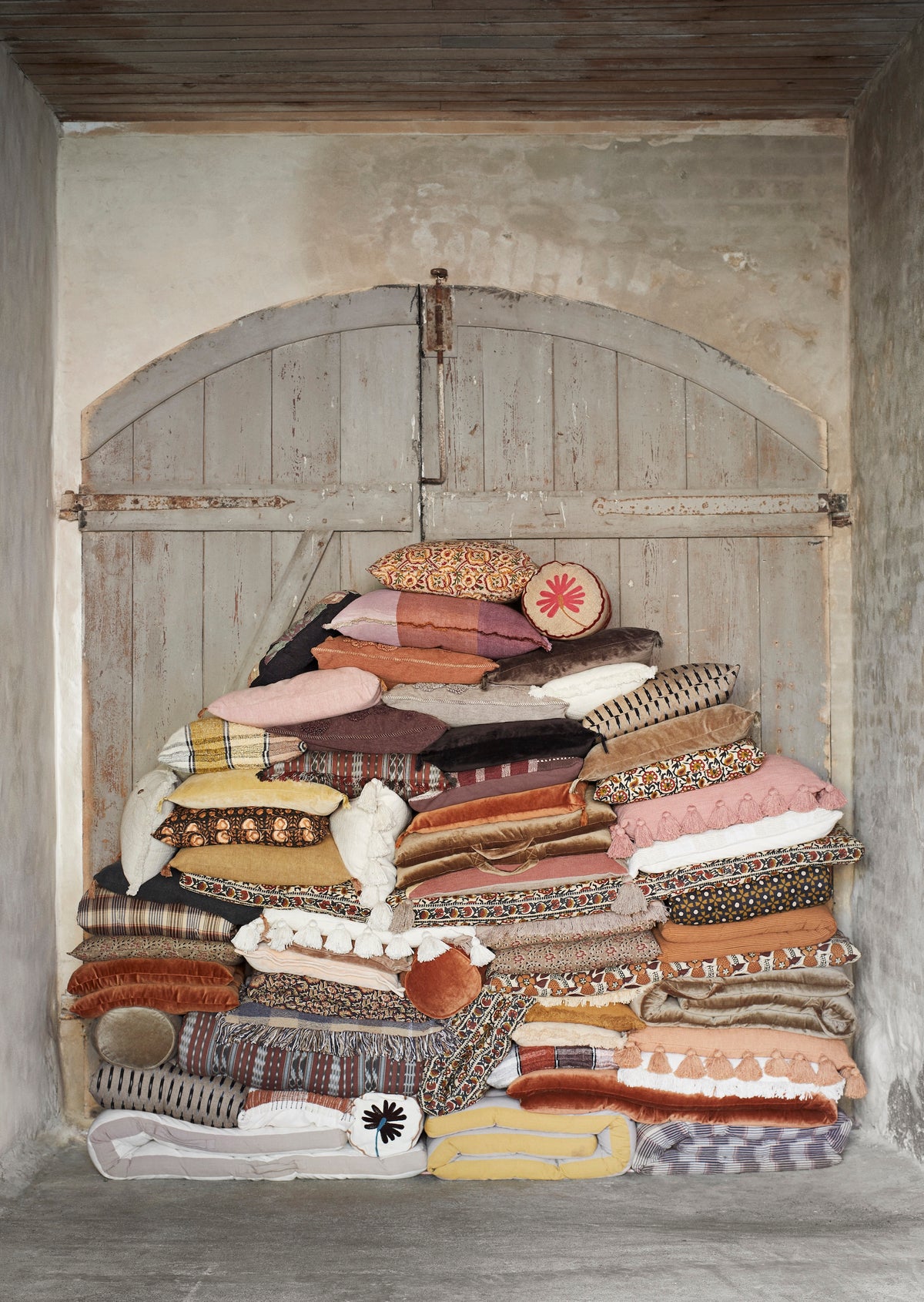stacked velvet and patterned cushions including burnt orange bolster in rustic Scandinavian interior
