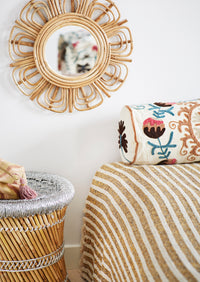 Decorative mirror with rattan frame above a bed with striped bedding and a patterned pillow.