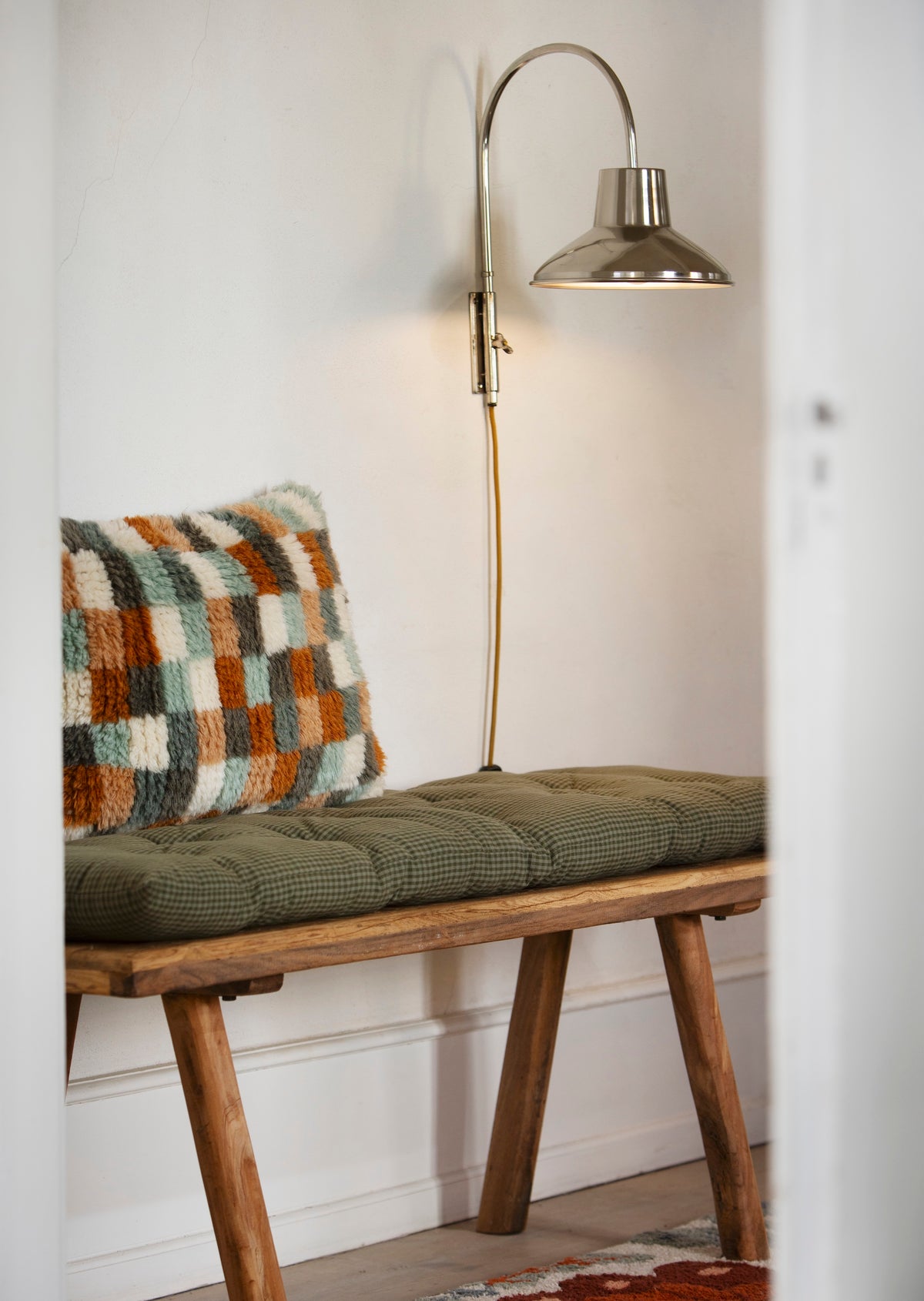 handwoven wool cushion in art deco colours styled on a wooden bench for Nordic hallway
