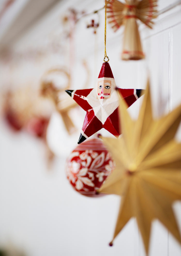 close up of wooden santa star ornament hanging on christmas garland
