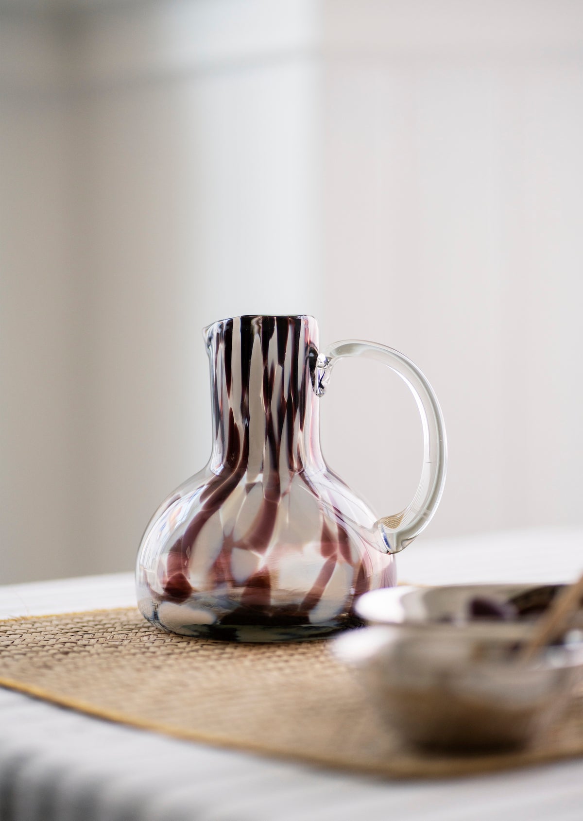 handmade coloured glass jug with brown pattern styled on a dining table
