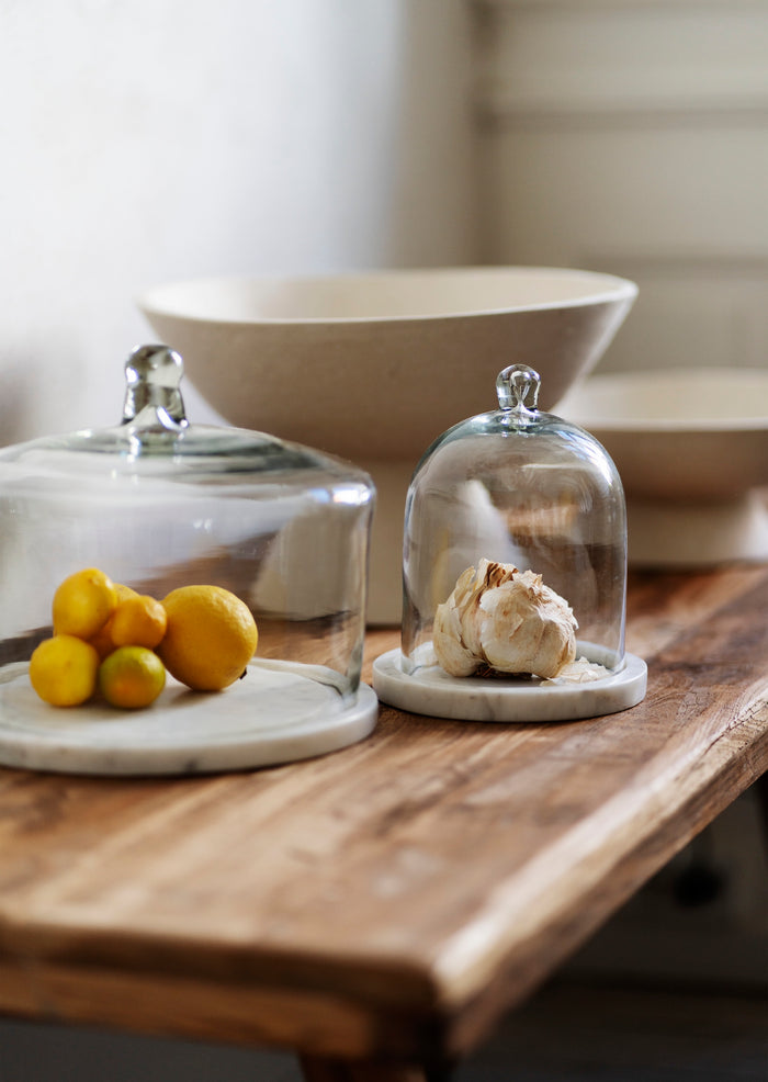 glass cloche with marble base styled on wooden counter with fruit
