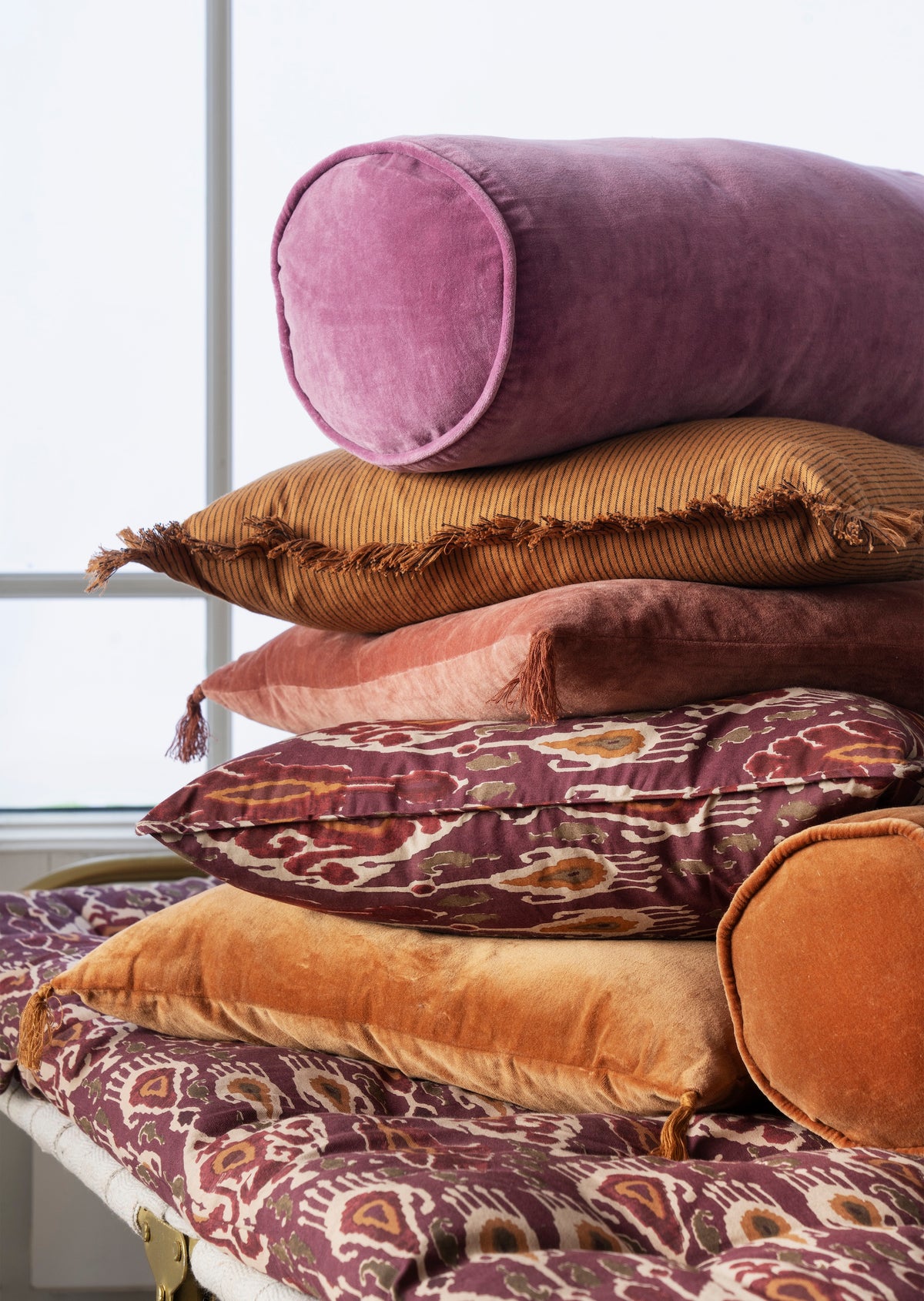 close-up of velvet bolster cushions in rich tones layered together for cosy styling
