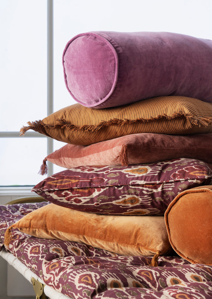 close-up of velvet bolster cushions in rich tones layered together for cosy styling
