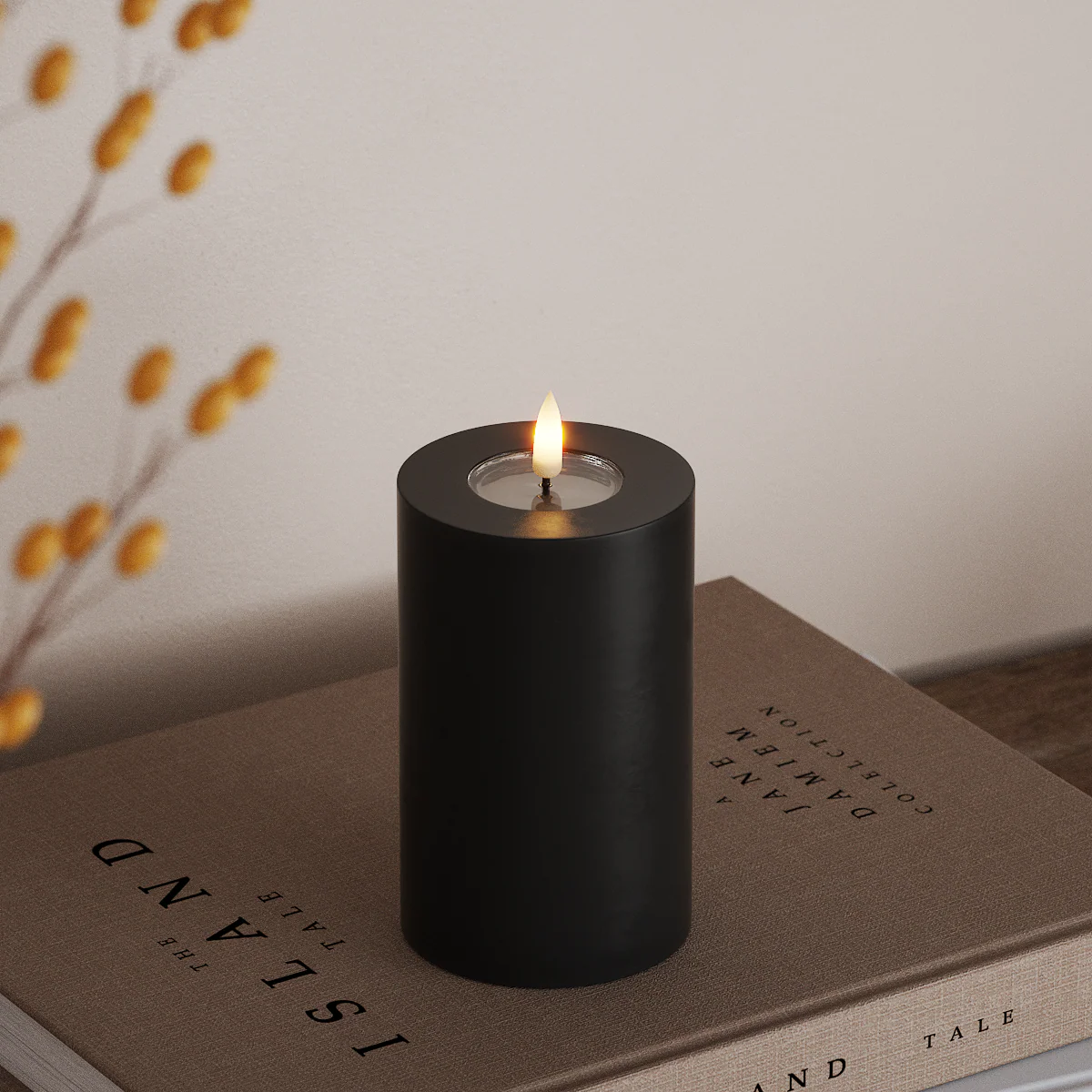 black wax-coated LED pillar candle with glowing flame on neutral books for cosy autumn styling