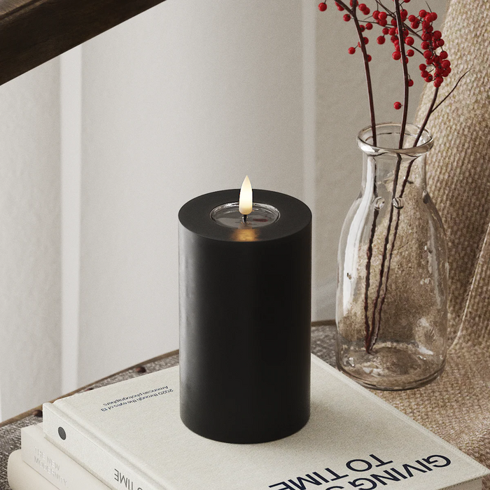 realistic black LED candle with flickering flame styled beside winter foliage on a tabletop