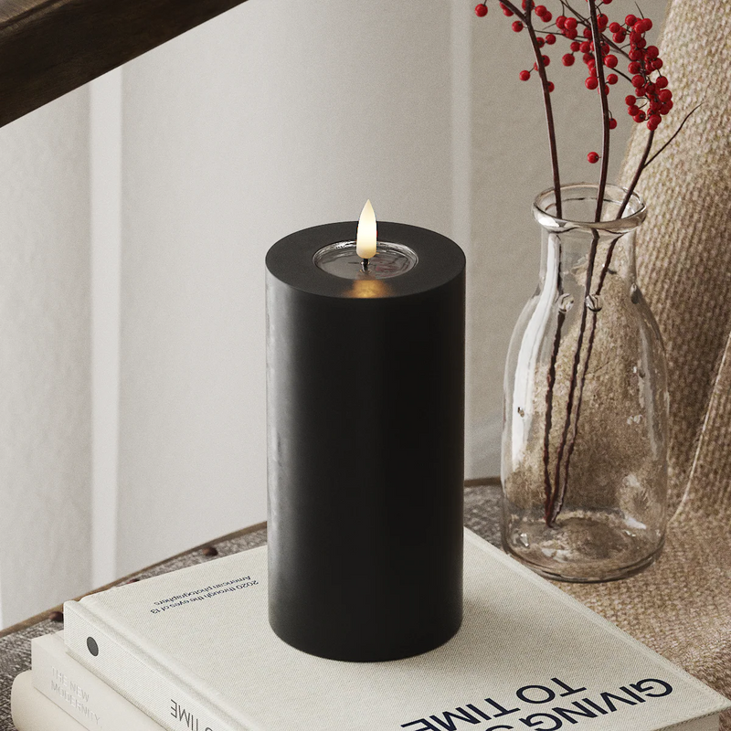 modern black LED candle with glowing flame on books for soft winter home lighting