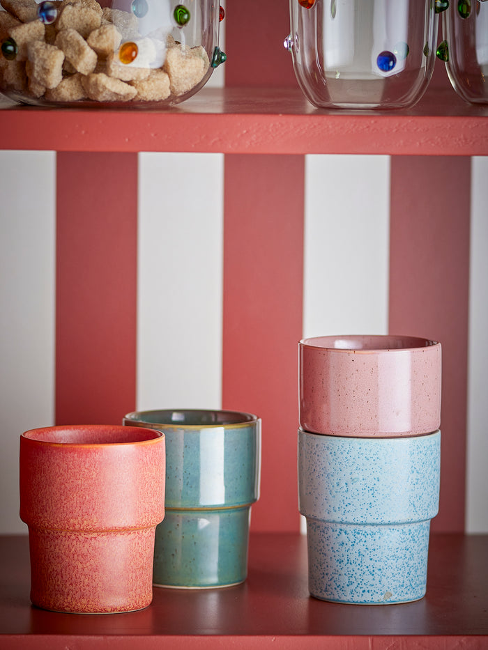 stacked bloomingville ewan stoneware cups in pastel colours on striped red and white kitchen shelf
